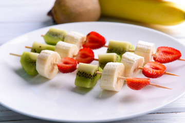 Fresh fruits on skewers in plate on table, closeup