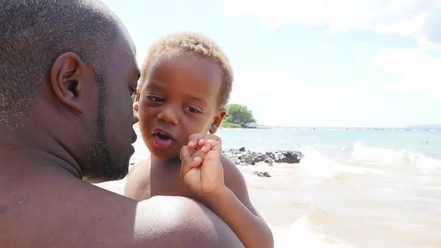 Black father holding his toddler on the beach