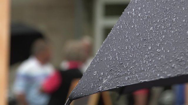 Close up of an umbrella full of raindrops with blurred people in the background.