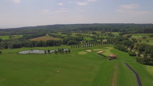 A drone flies above a golf course filming the landscpae around on a sunny day.