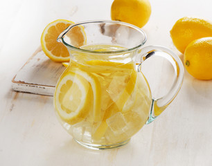 Water with lemon and ice in a glass jug.