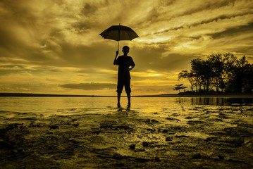 image silhouette a boy standing holding an umbrella during sunset sunrise. sand and tree with soft cloud on sky