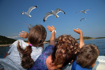 The children are feeding and waving the seagull on the boat