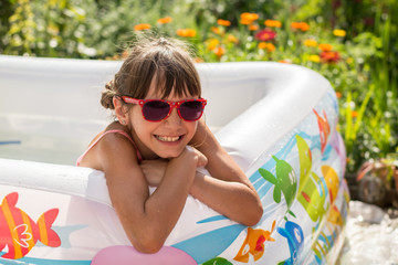 Cute little girl in sunglasses awash in an inflatable pool in the garden