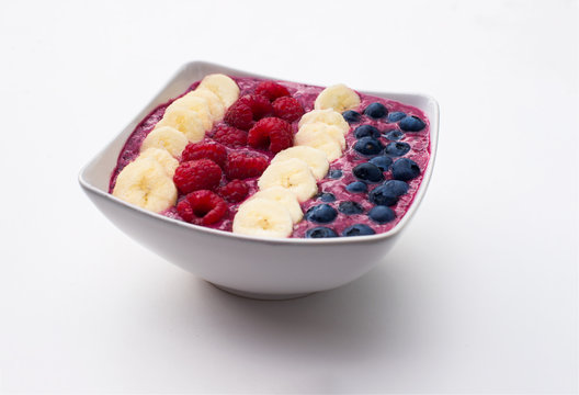 berry smoothie bowl on white background, topped with bananas, raspberries and blueberries