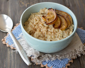 Oatmeal with baked apples and cinnamon in blue ceramic bowl on wooden table