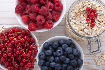 berries, fruit and muesli ingredients for healthy breakfast on white wooden table