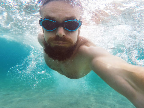 Young bearded man diving in a blue clean water