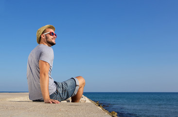 Happy man sitting by the sea with hat