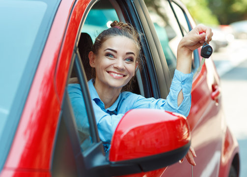 Young cheerful woman sitting in a car with keys in hand