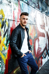 Attractive young man in white shirt and black jacket on graffiti background