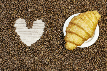 Coffee bean background with heart and croissant on white plate o