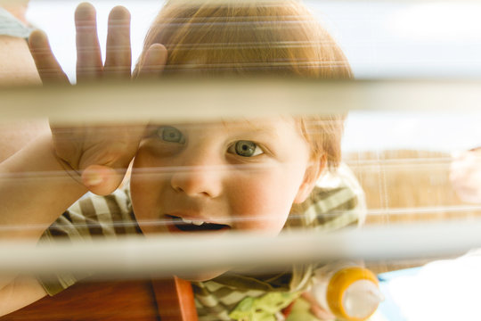 Kleiner Junge blickt durch Jalousie in Wohnung