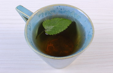 Lemon balm in cup of herbal drink on white wooden table