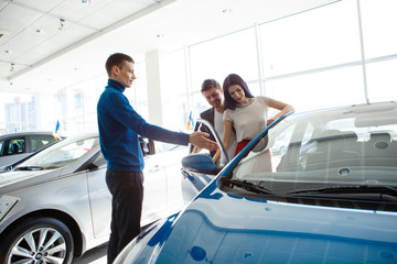 mature salesman showing new car to  couple in showroom