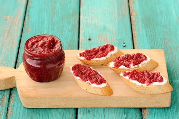 Homemade sweet raspberry jam in glass jar with four toasts with