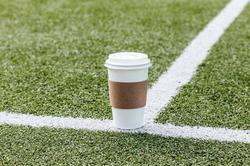 Blank coffee paper cup on football field