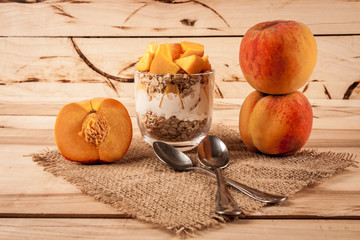 Obraz na płótnie Canvas Healthy breakfast - yogurt with fresh peach and muesli served in glass jar, on wooden background