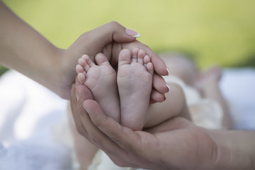 Happy family of mother and father touching bare feet with little toys and soft skin of small tiny baby with male and female hands outdoor closeup, hotizontal picture