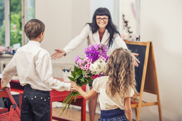 Boy and girl children give flowers as a school teacher in teache