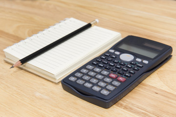 calculator, note and pencil on wood background