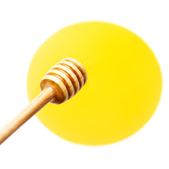 Wooden honey dipper with yellow honey flowing drops isolated on