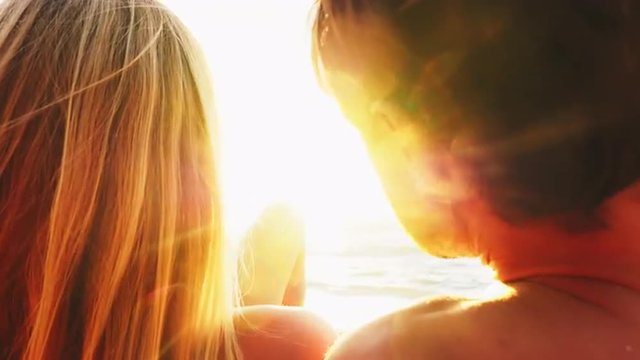 Couple lie on a beach and look out over the ocean at sunset