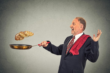 Happy smiling senior man tossing pancakes on frying pan