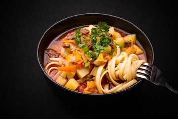 Uzbek noodle soup Lagman on black, close up