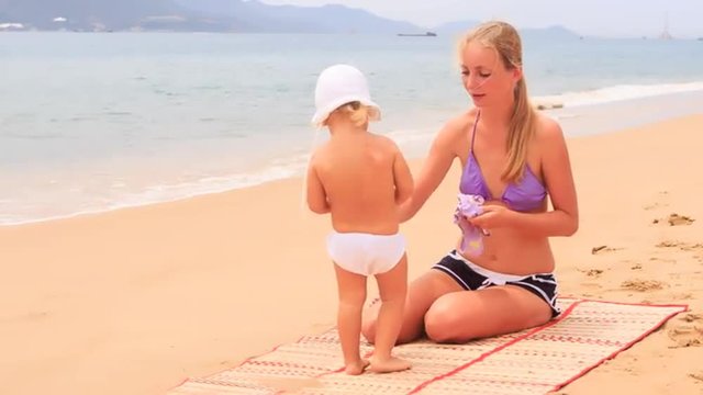 mother shows swimsuit to daughter sitting on sandy beach	