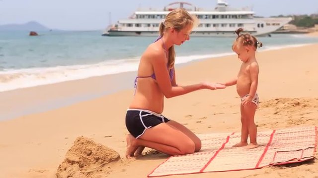 young mother play with little daughter at mat on beach	