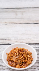 Deep fried shallots for garnishing in white bowl over wooden background