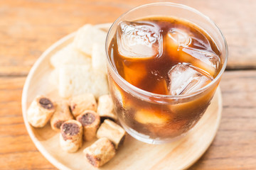 Glass of black iced coffee with some snack