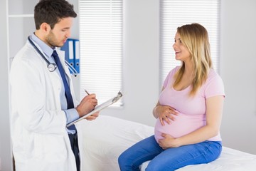 Fototapeta premium Smiling pregnant patient talking to doctor which is taking notes