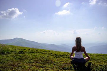 Young blonde woman meditating at the mountain peak