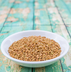 Fenugreek seeds in white bowl over wooden background