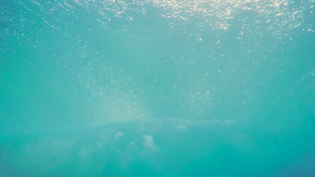 Looking Through a Blue Ocean Wave From Underwater as it Crashes onto the Beach with Sunrise Light.