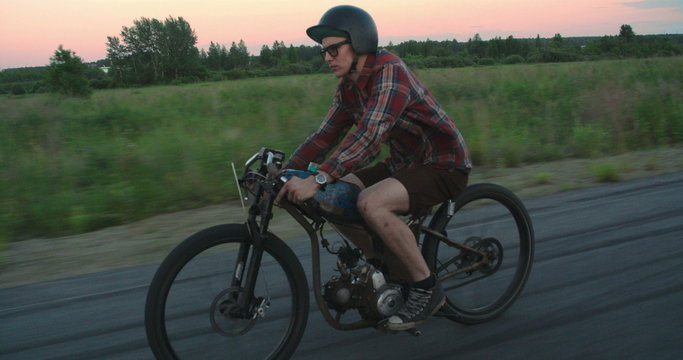 Side view of a young guy in helmet driving a scooter along the countryside road