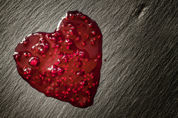 Drops of red raspberry jam in the form of heart on the black sto