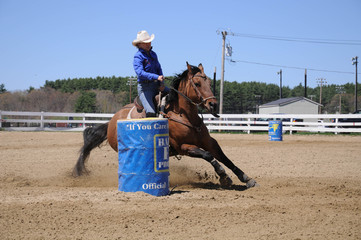 Young blonde woman barrel racing; A young woman turns around a barrel before racing to the finish...