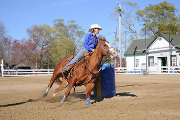 Young blonde woman barrel racing ; A young woman turns around a barrel and begins racing to the...