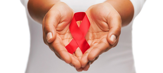 hands holding red AIDS awareness ribbon - obrazy, fototapety, plakaty