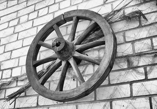 Antique wooden wagon wheel hanging on a brick wall.