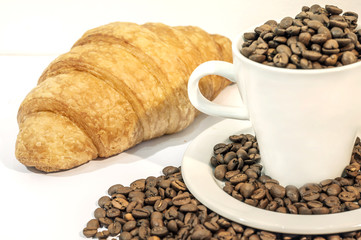 Cup of coffee filed with coffee beans with croissants on white b