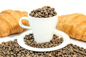 Cup of coffee filed with coffee beans with two croissants on whi