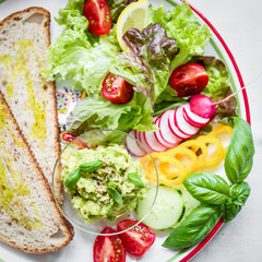 Plate with bread, smashed avocado and fresh vegetables