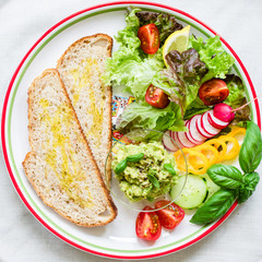 Plate with bread, smashed avocado and fresh vegetables