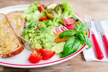 Plate with bread, smashed avocado and fresh vegetables
