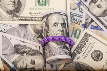 Hundred dollar bills rolled up with rubberband on dollars background 