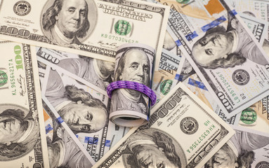 Hundred dollar bills rolled up with rubberband on dollars background 